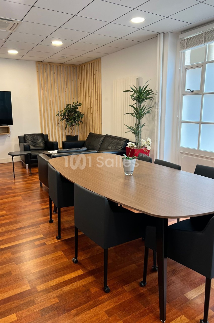 Salle lumineuse avec table en bois, chaises noires, canapé, plantes et parquet en bois.