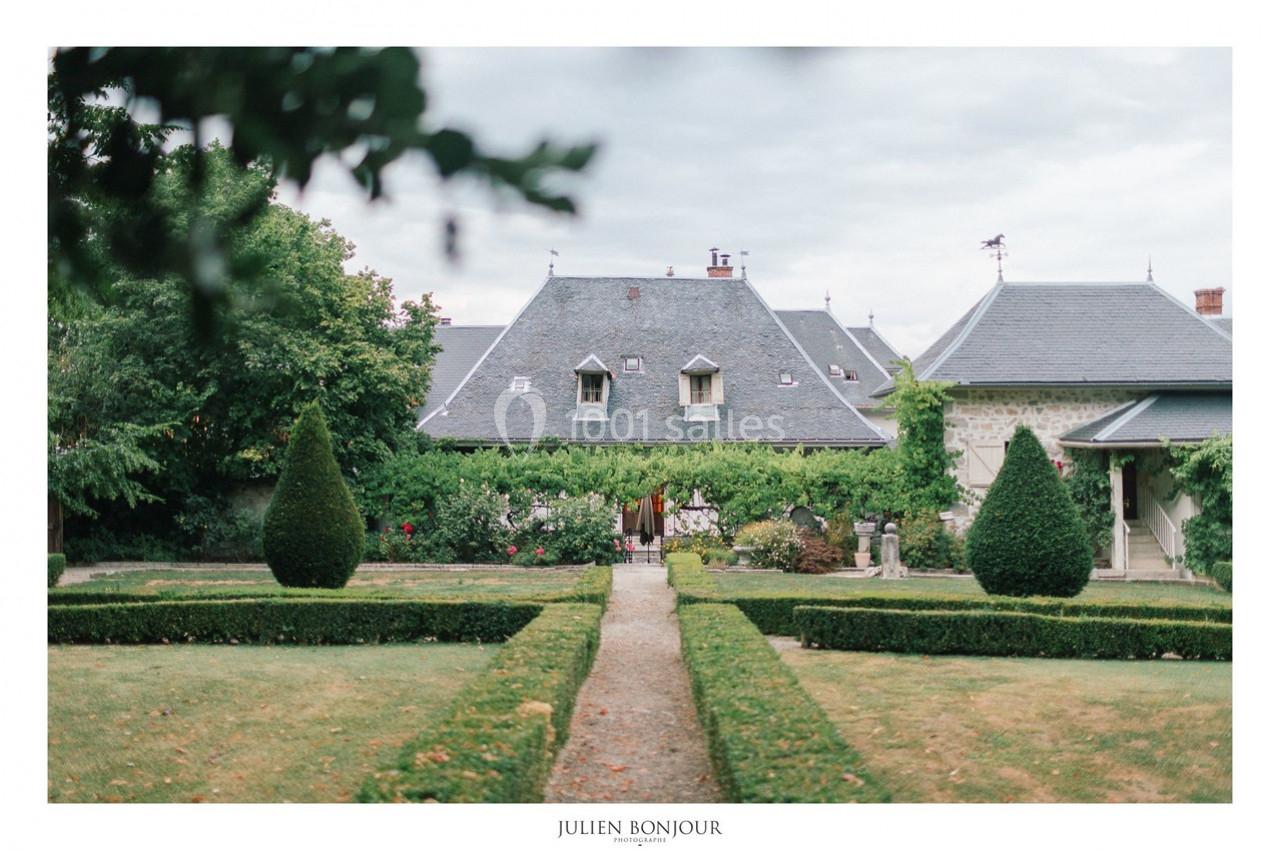 Jardin symétrique avec allée centrale menant à une maison en pierre couverte de lierre, sous un ciel nuageux.