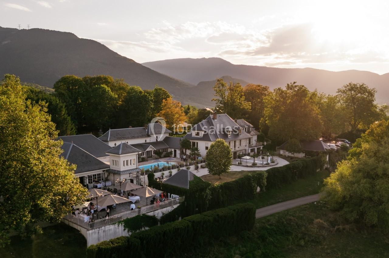 Vue aérienne d'un domaine avec piscine, entouré de verdure et de montagnes au coucher du soleil.