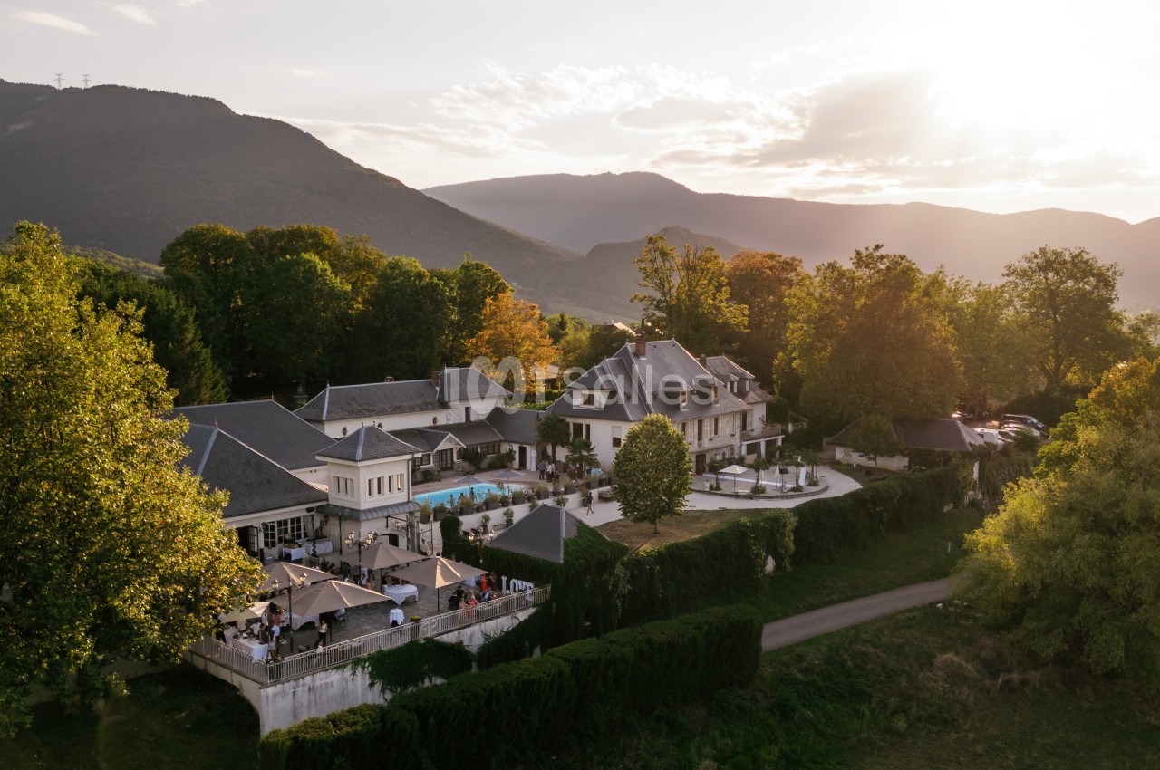 Vue aérienne d'un domaine avec piscine, entouré de verdure et de montagnes au coucher du soleil.