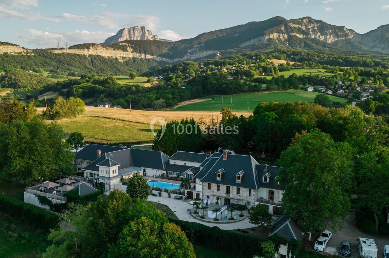 Vue aérienne d'un domaine entouré de verdure, avec des montagnes en arrière-plan sous un ciel dégagé.