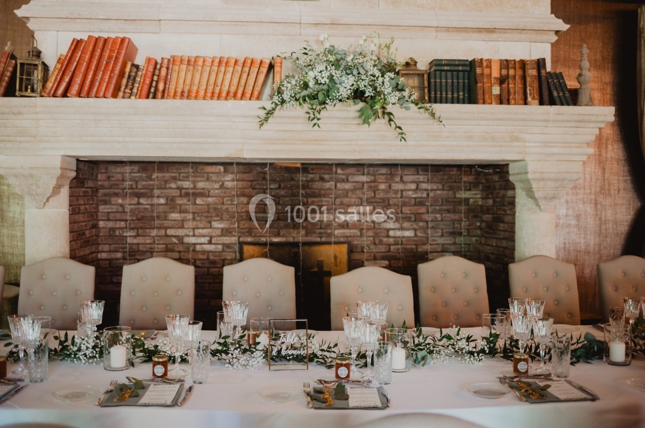 Table décorée pour un repas élégant, devant une cheminée ornée de livres anciens et de fleurs.