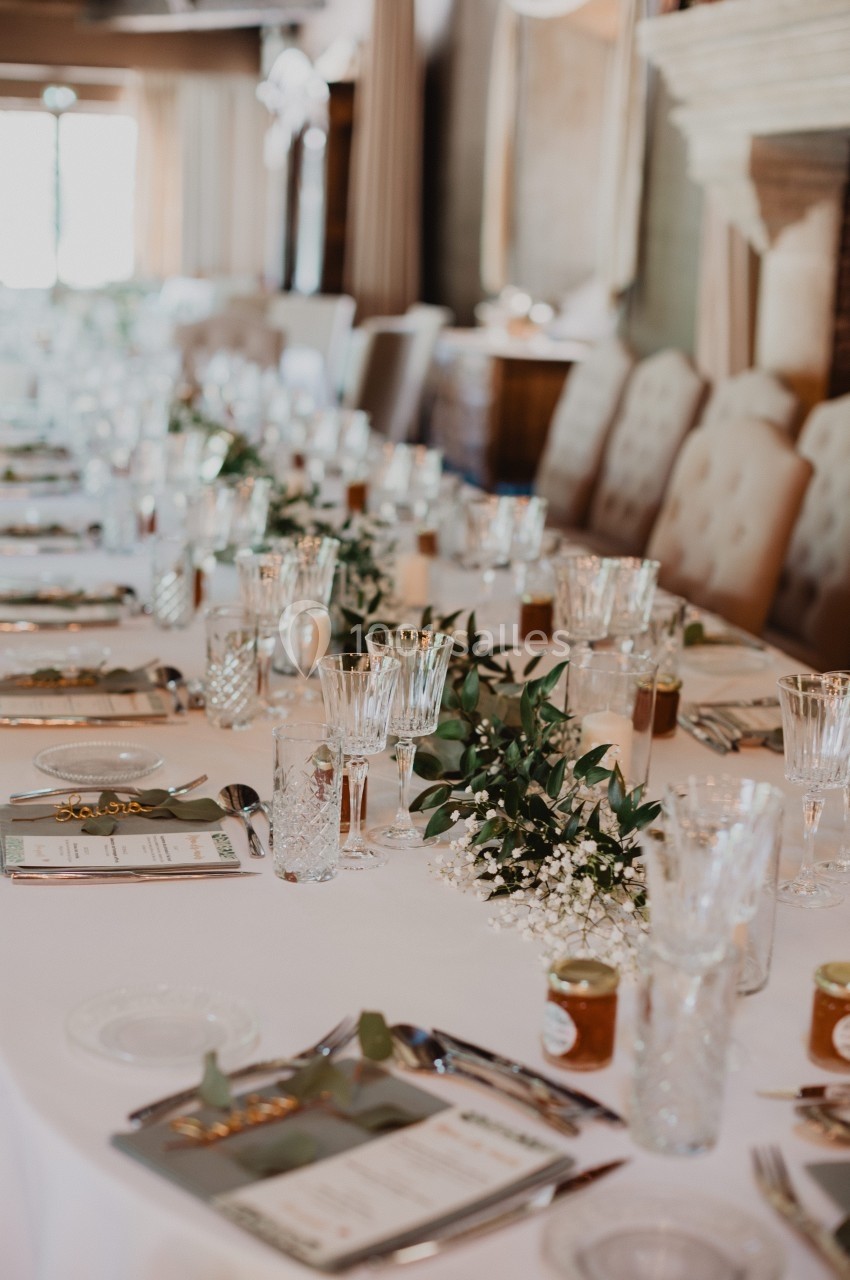 Table élégamment dressée avec nappes blanches, verres en cristal, menus et décoration florale.