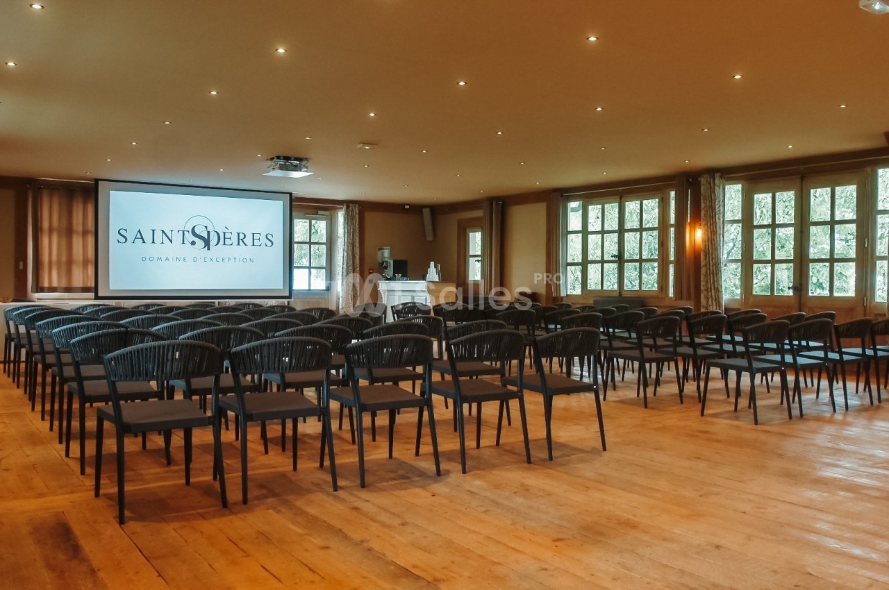 Salle de conférence lumineuse avec rangées de chaises noires, écran de projection et parquet en bois clair.