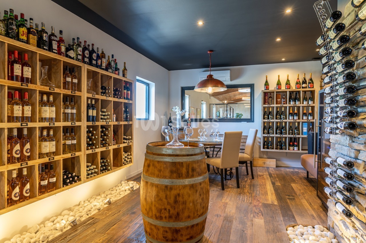 Salle de dégustation avec étagères de bouteilles de vin, tonneau en bois au centre et table dressée en arrière-plan.