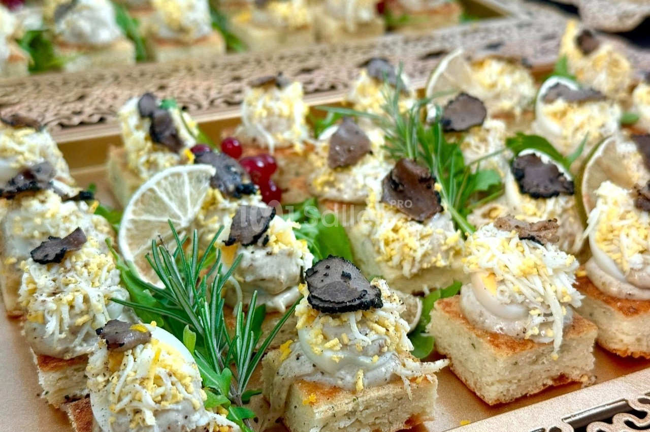 Plateau de canapés garnis de mousse, truffes, herbes fraîches, citron et groseilles rouges en décoration.