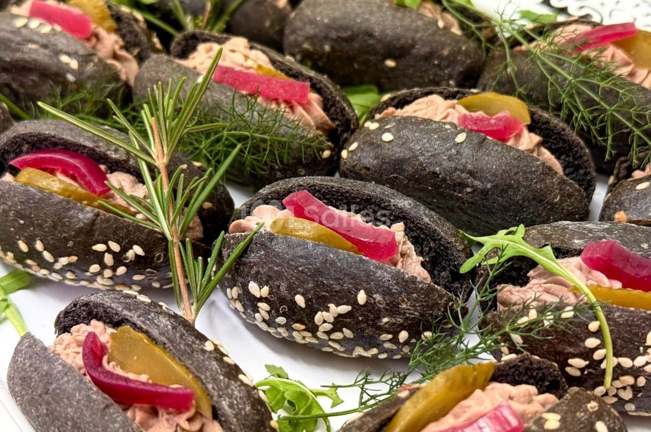Mini pains noirs garnis de rillettes, cornichons, pickles rouges et décorés de graines de sésame et herbes fraîches.