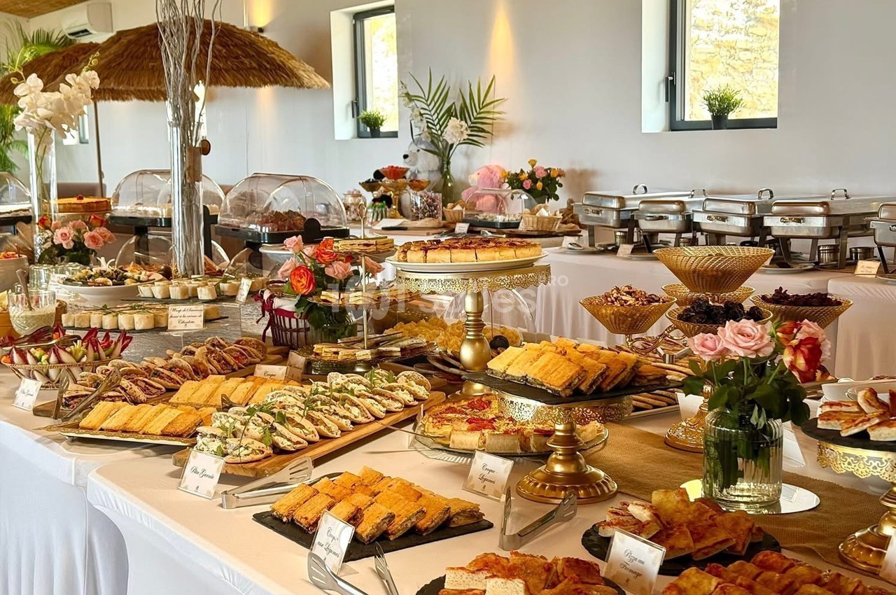 Buffet varié avec plats salés, desserts et décorations florales dans une salle lumineuse.