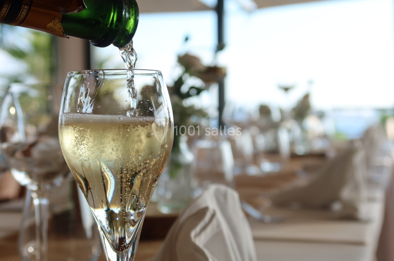 Un verre de champagne est rempli sur une table élégamment dressée avec des serviettes et des fleurs en arrière-plan.