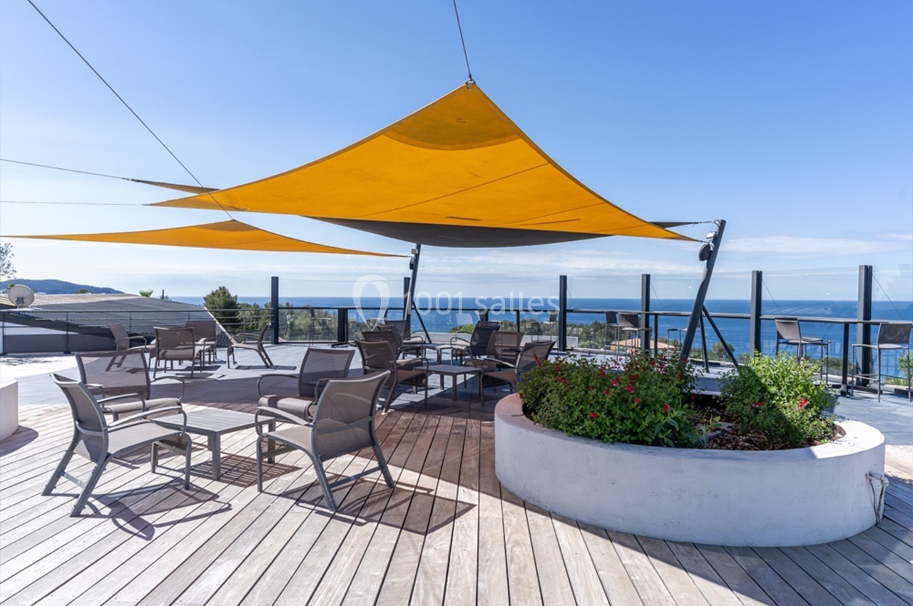 Terrasse en bois avec voiles d'ombrage jaunes, mobilier de jardin et vue sur la mer à l'arrière-plan.