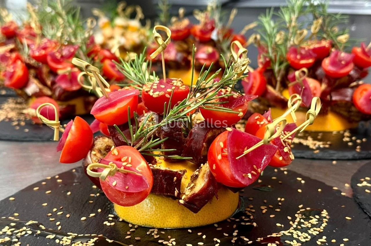 Assiette de présentation avec brochettes de tomates cerises, dattes et romarin sur une base d'orange, décorée de graines de…