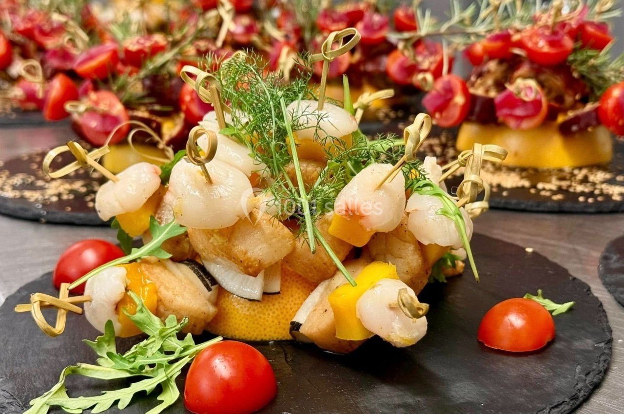 Assiette de brochettes de fruits de mer avec herbes fraîches, tomates cerises et roquette sur une ardoise noire.