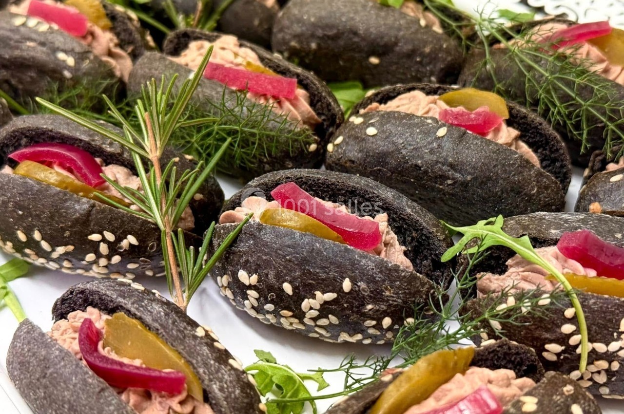 Mini pains noirs garnis de pâté, cornichons, oignons rouges marinés, herbes fraîches et graines de sésame.
