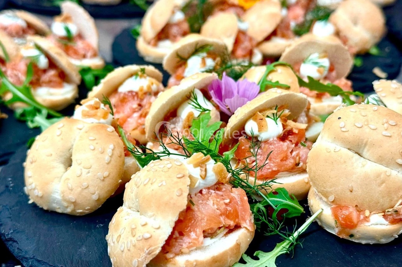 Mini bagels garnis de saumon fumé, fromage frais, aneth et roquette, présentés sur un plateau en ardoise.