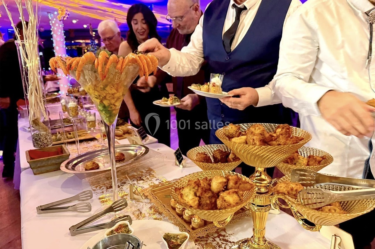 Buffet élégant avec verrines de crevettes et assortiments de bouchées dorées, des convives se servant.