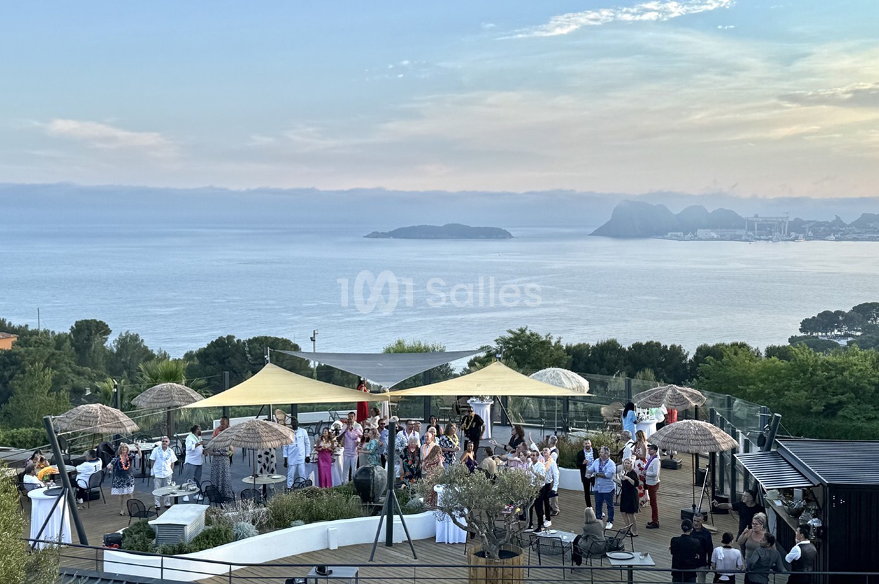 Groupe de personnes réunies sur une terrasse en bord de mer, avec vue sur l'horizon et des îles au loin.