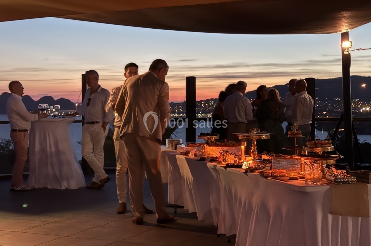 Groupe de personnes discutant près d'un buffet lors d'un événement en soirée avec vue sur un paysage au coucher du soleil.