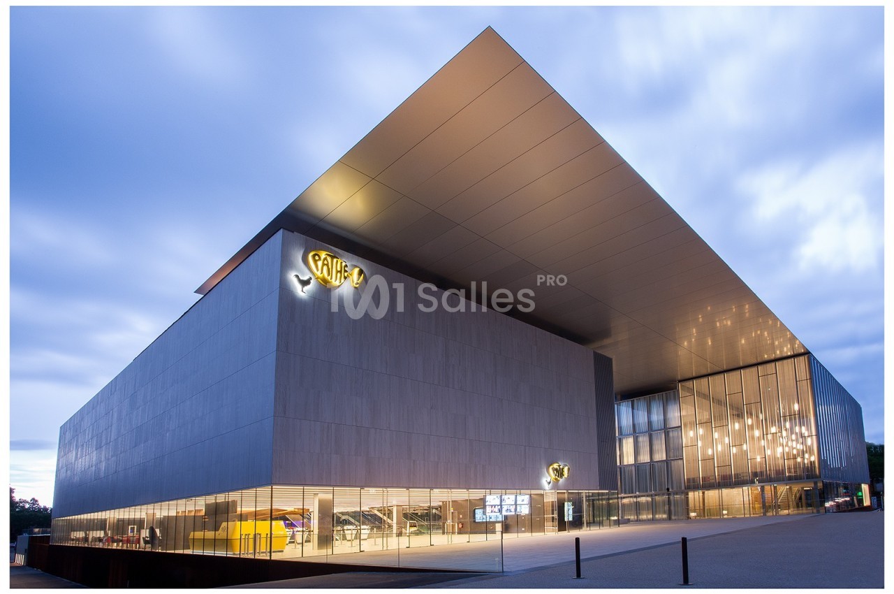 Bâtiment moderne avec façade en verre et métal, éclairé en soirée, portant le logo d'un cinéma Pathé.