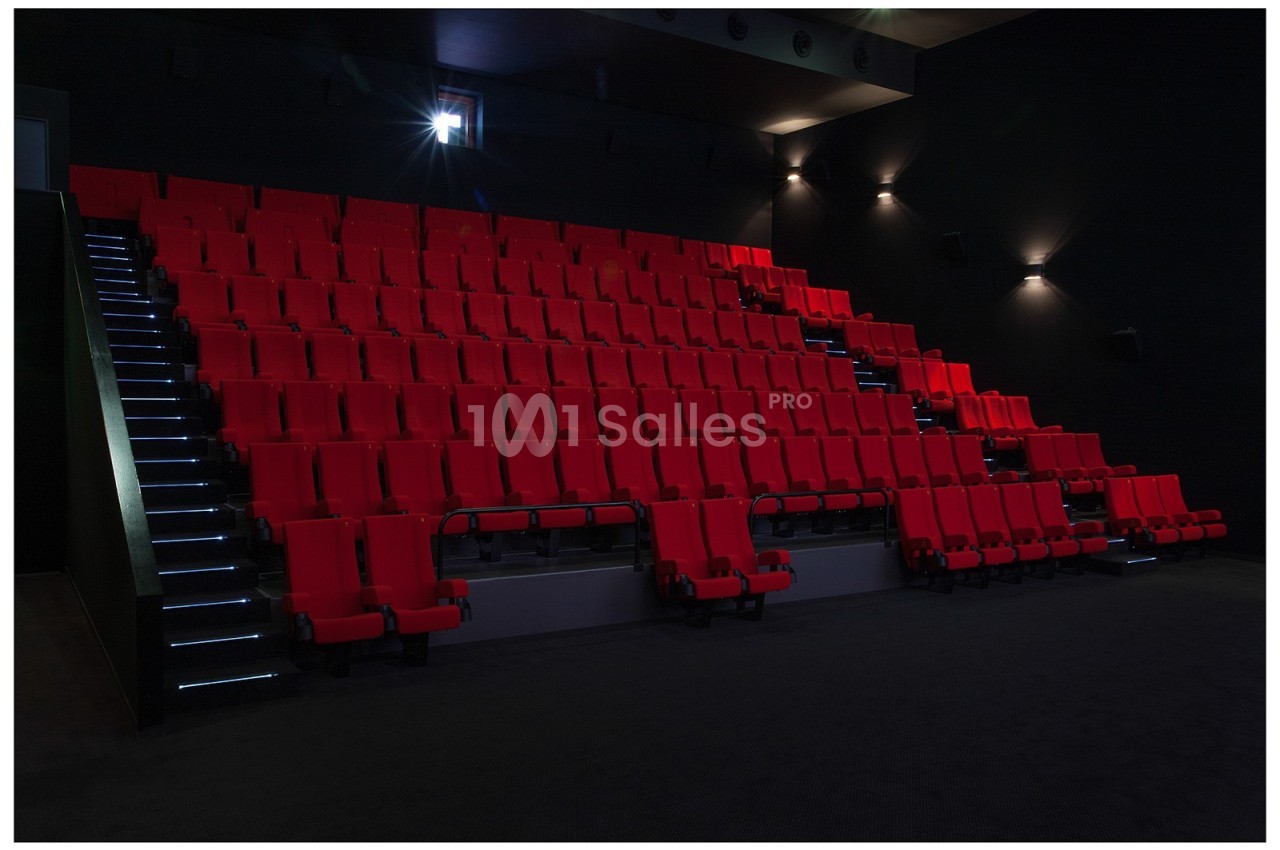 Salle de cinéma vide avec des rangées de sièges rouges et un éclairage tamisé.