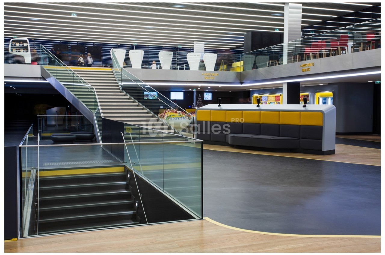 Intérieur moderne avec escalier, sièges jaunes et noirs, éclairage linéaire au plafond et espace ouvert.