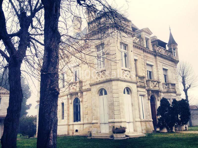Manoir en pierre avec des fenêtres ornées, entouré d'arbres dénudés et d'une pelouse verte par temps brumeux.