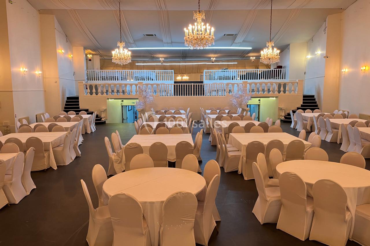 Salle de réception spacieuse avec tables rondes et chaises blanches, éclairée par des lustres et appliques murales.