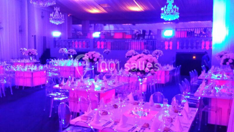 Salle de réception décorée avec des tables dressées, des chaises transparentes et un éclairage violet.