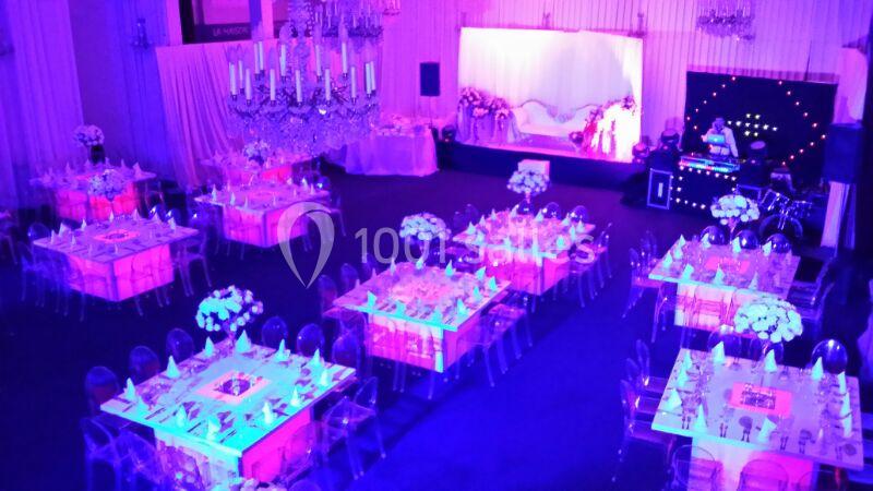 Salle de réception décorée avec des tables illuminées en rose, des chaises transparentes et un éclairage tamisé.
