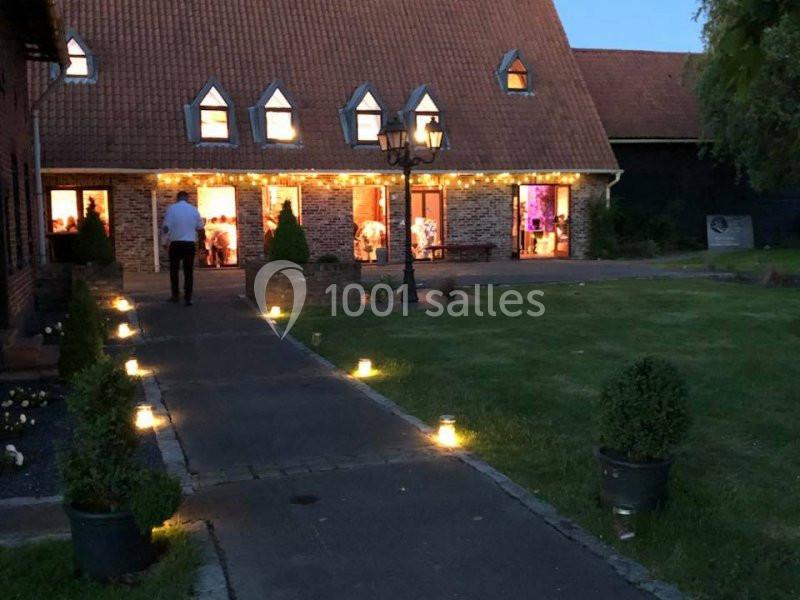Location salle Watten (Nord) - Le Domaine du Fil de l’Eau #21 Allée éclairée menant à une maison en briques avec toit en pente, décorée de guirlandes lumineuses en soirée.