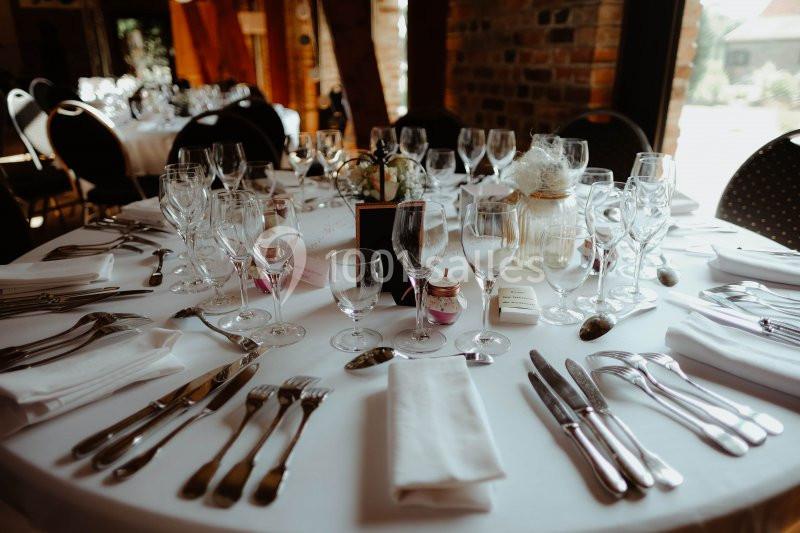 Location salle Watten (Nord) - Le Domaine du Fil de l’Eau #15 Table ronde élégamment dressée avec nappes blanches, verres, couverts et décoration florale dans une salle lumineuse.