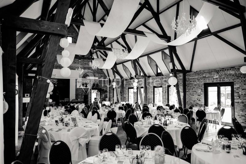 Location salle Watten (Nord) - Le Domaine du Fil de l’Eau #13 Salle de réception avec poutres apparentes, tables dressées et décorations suspendues dans un style élégant.