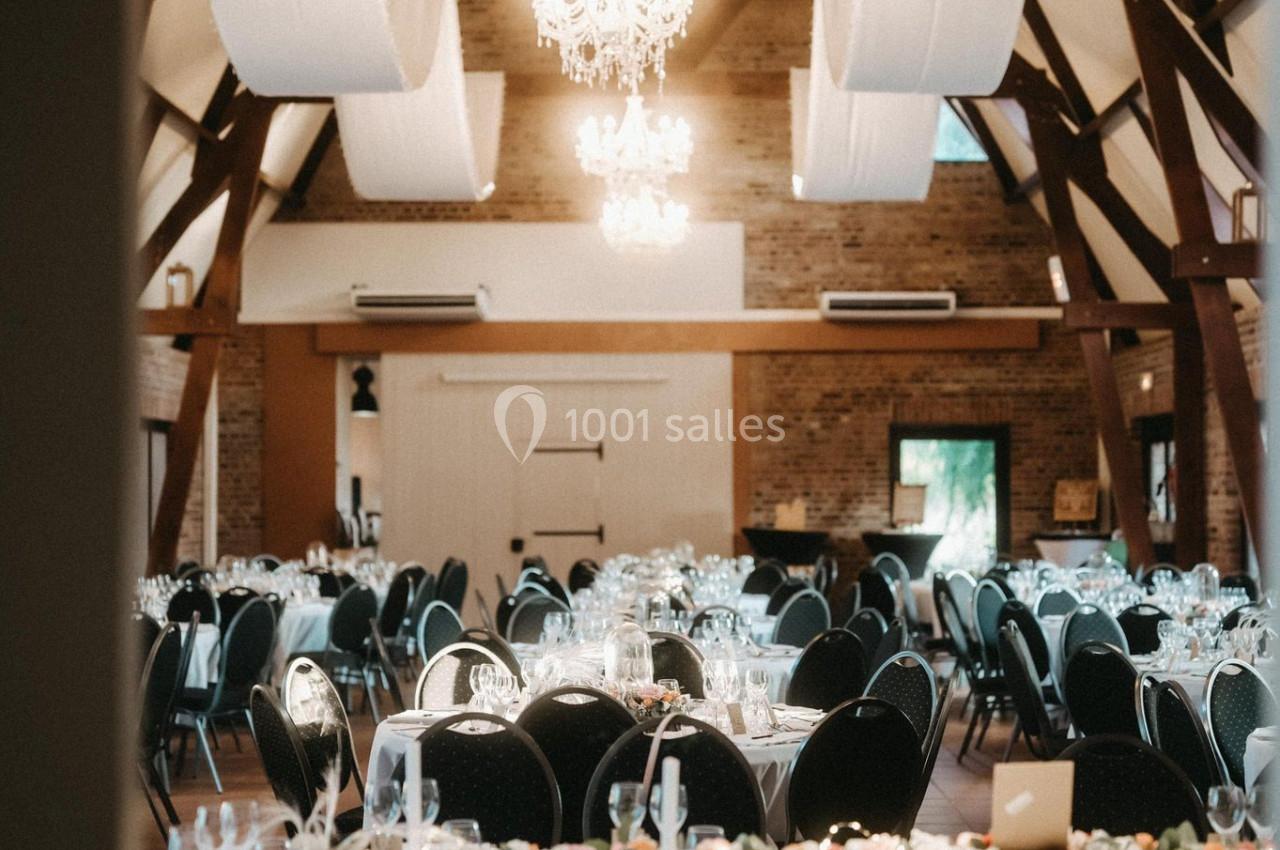 Location salle Watten (Nord) - Le Domaine du Fil de l’Eau #3 Salle de réception élégante avec tables rondes décorées, chaises noires et lustres suspendus sous une charpente en bois.