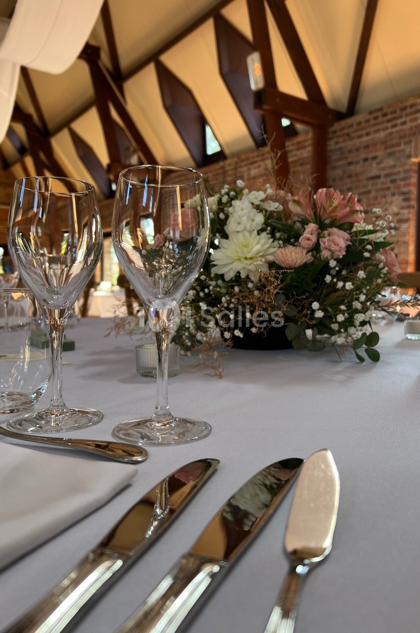 Table élégamment dressée avec des verres à vin, des couverts brillants et un centre de table floral dans une salle en…