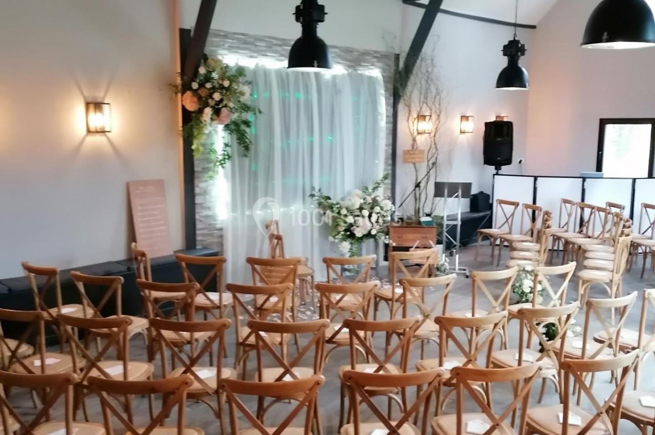 Location salle Watten (Nord) - Le Domaine du Fil de l’Eau #8 Salle de réception décorée pour une cérémonie, avec des chaises en bois disposées face à une arche fleurie.