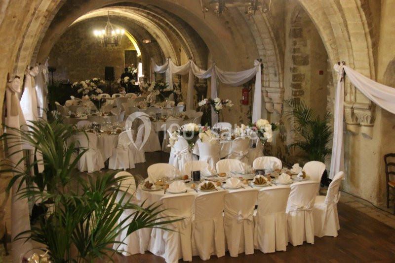 Salle voûtée décorée pour un mariage, avec tables rondes dressées, nappes blanches et arrangements floraux.