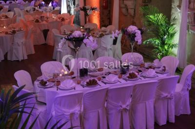 Château en pierre éclairé par des lampadaires au crépuscule, entouré d'arbres et d'une allée gravillonnée.