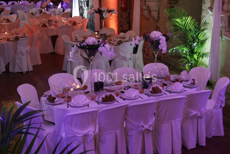 Salle de réception décorée avec des tables élégantes, nappes blanches, fleurs et éclairage tamisé.
