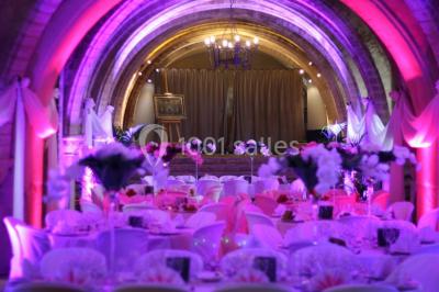 Château en pierre éclairé par des lampadaires au crépuscule, entouré d'arbres et d'une allée gravillonnée.