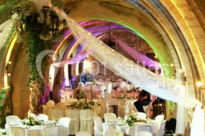 Château en pierre éclairé par des lampadaires au crépuscule, entouré d'arbres et d'une allée gravillonnée.