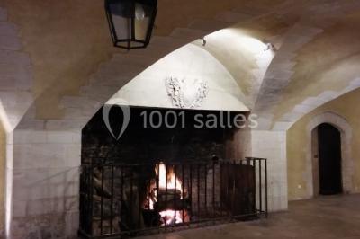 Château en pierre éclairé par des lampadaires au crépuscule, entouré d'arbres et d'une allée gravillonnée.