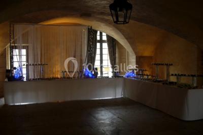 Château en pierre éclairé par des lampadaires au crépuscule, entouré d'arbres et d'une allée gravillonnée.