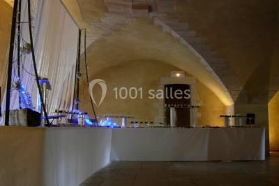 Château en pierre éclairé par des lampadaires au crépuscule, entouré d'arbres et d'une allée gravillonnée.