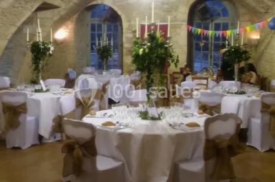 Château en pierre éclairé par des lampadaires au crépuscule, entouré d'arbres et d'une allée gravillonnée.