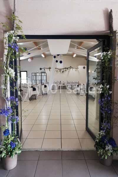 Vue d'une salle de réception décorée avec des fleurs bleues et blanches, tables dressées et guirlandes suspendues.