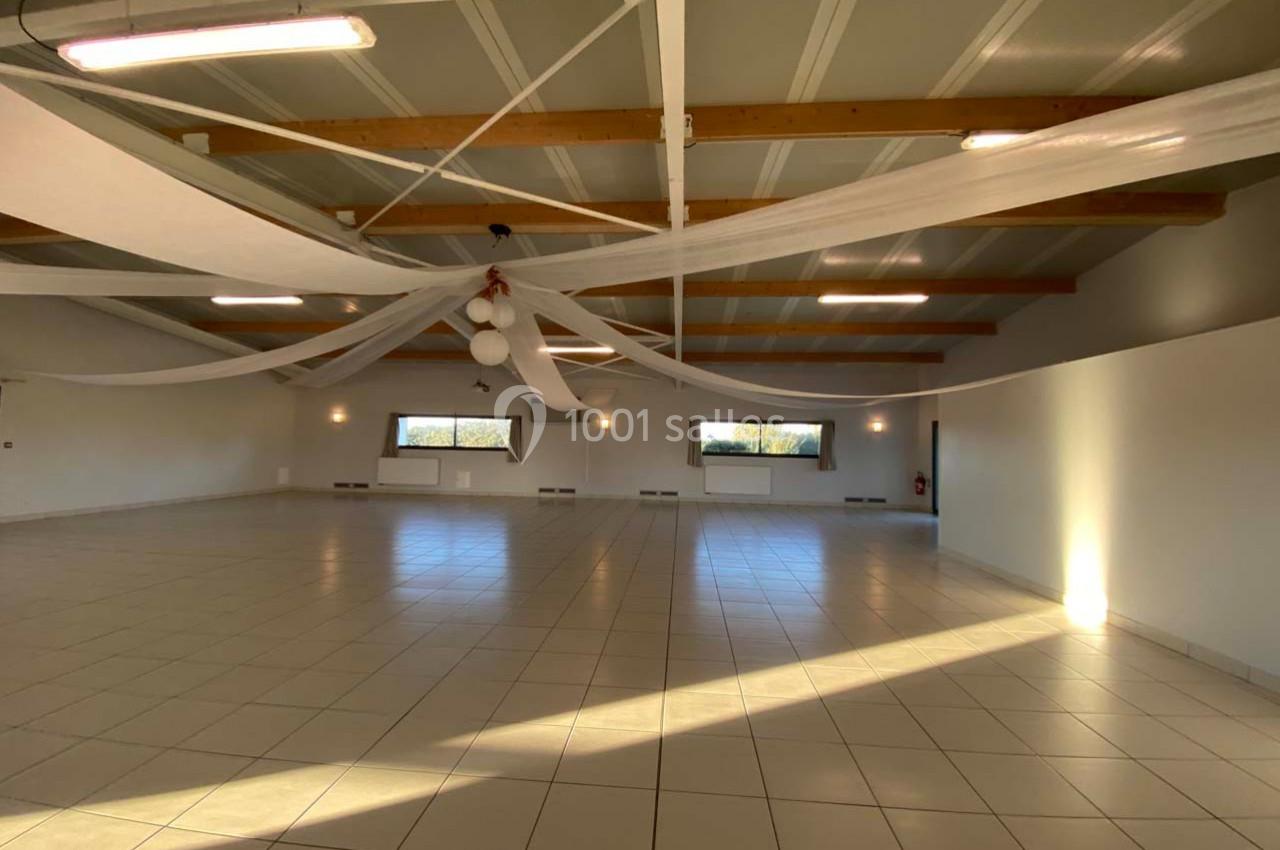 Salle spacieuse avec carrelage clair, plafond en poutres apparentes et décorations suspendues, éclairée par des fenêtres.