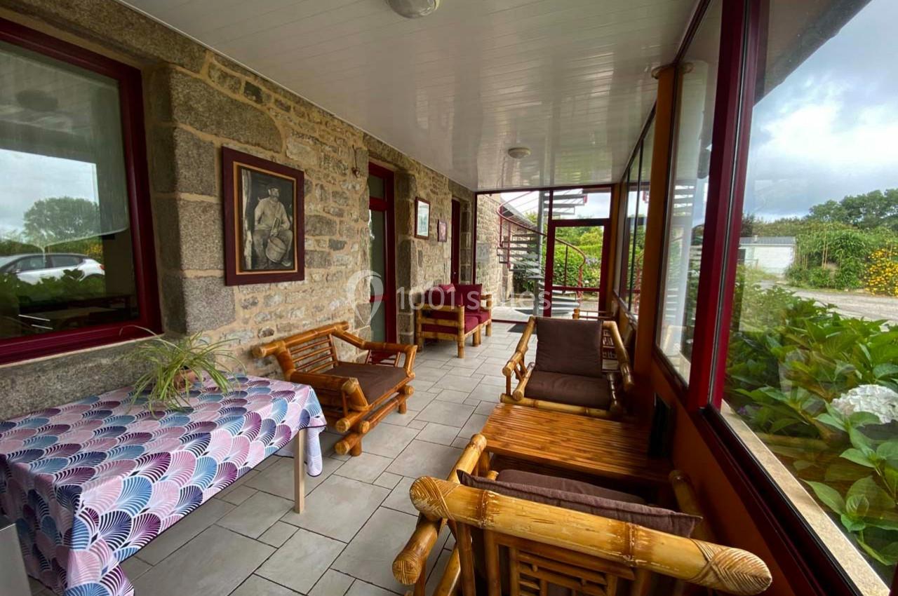Terrasse couverte avec murs en pierre, mobilier en bois, table décorée et vue sur un jardin verdoyant.