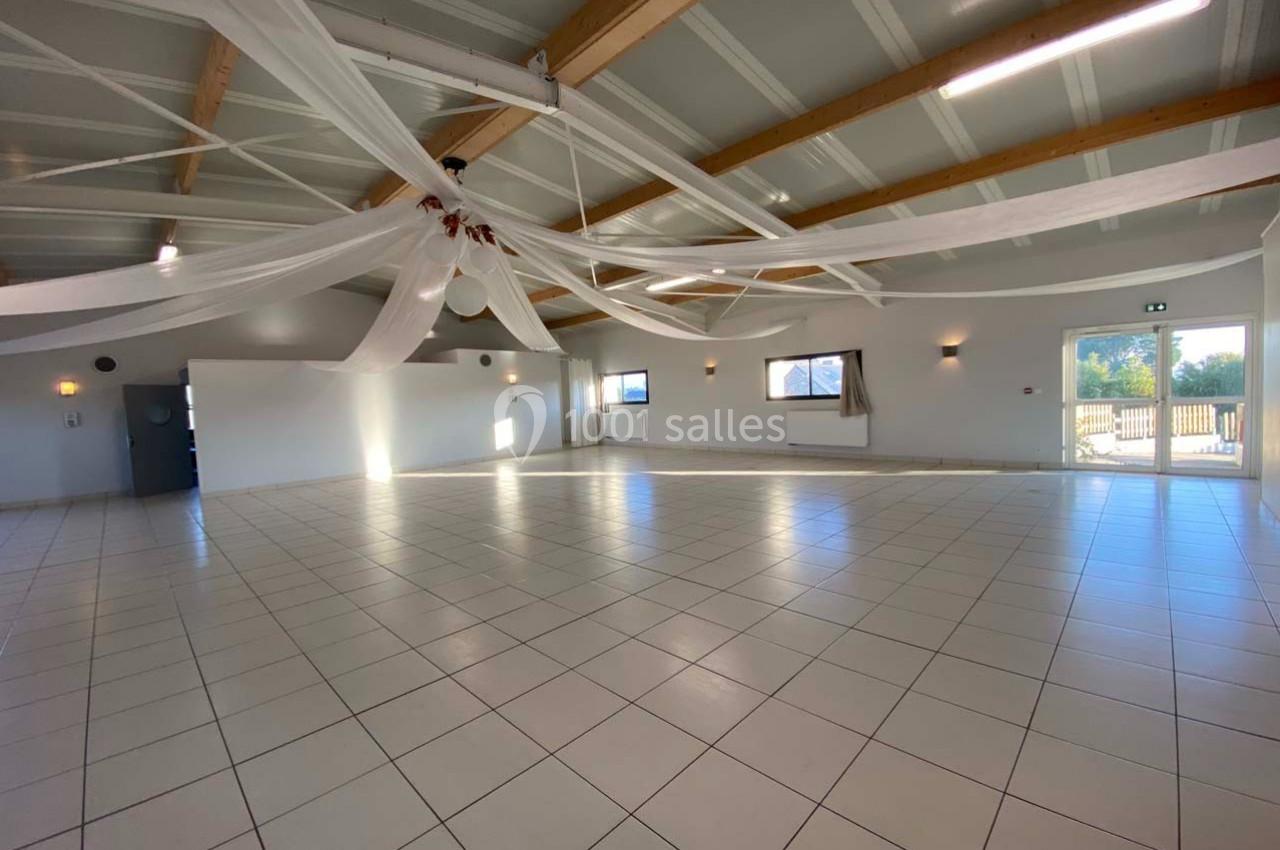 Salle spacieuse avec carrelage blanc, plafond en poutres apparentes et décorations suspendues, éclairée par la lumière…