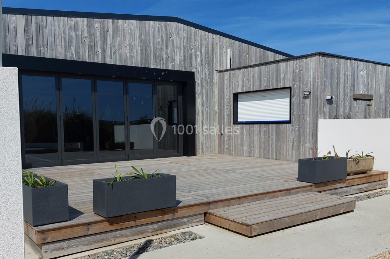 Terrasse en bois avec jardinières modernes devant une maison en bardage bois et grandes baies vitrées.