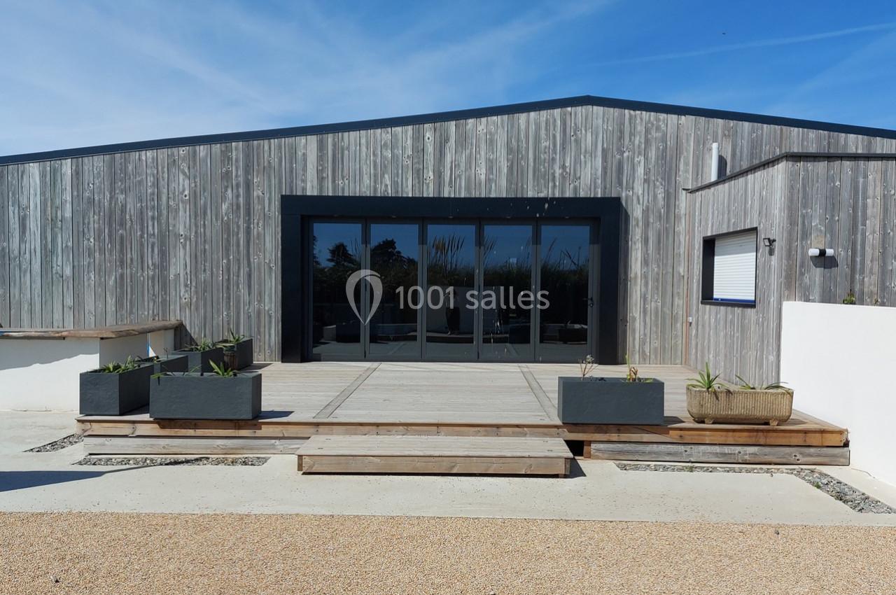 Façade d'un bâtiment moderne en bois avec une terrasse en béton, des jardinières et un ciel dégagé en arrière-plan.