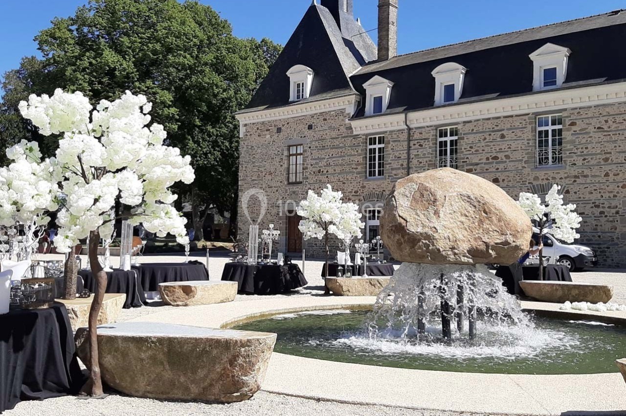 Fontaine entourée de tables décorées et d'arbres artificiels blancs devant un bâtiment en pierre sous un ciel dégagé.